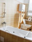 Łazienka dla mieszkańców. Na ścianach kremowe płytki ceramiczne. W centralnej części wanna. W tle okno przesłonięte poziomymi żaluzjami
